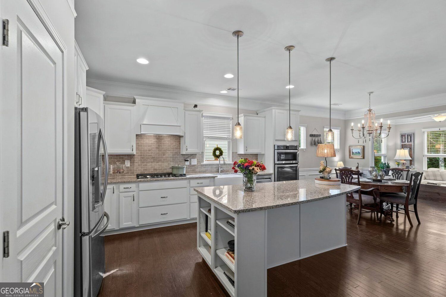 Bright kitchen with white cabinetry, granite island, stainless appliances, and an adjoining dining area.