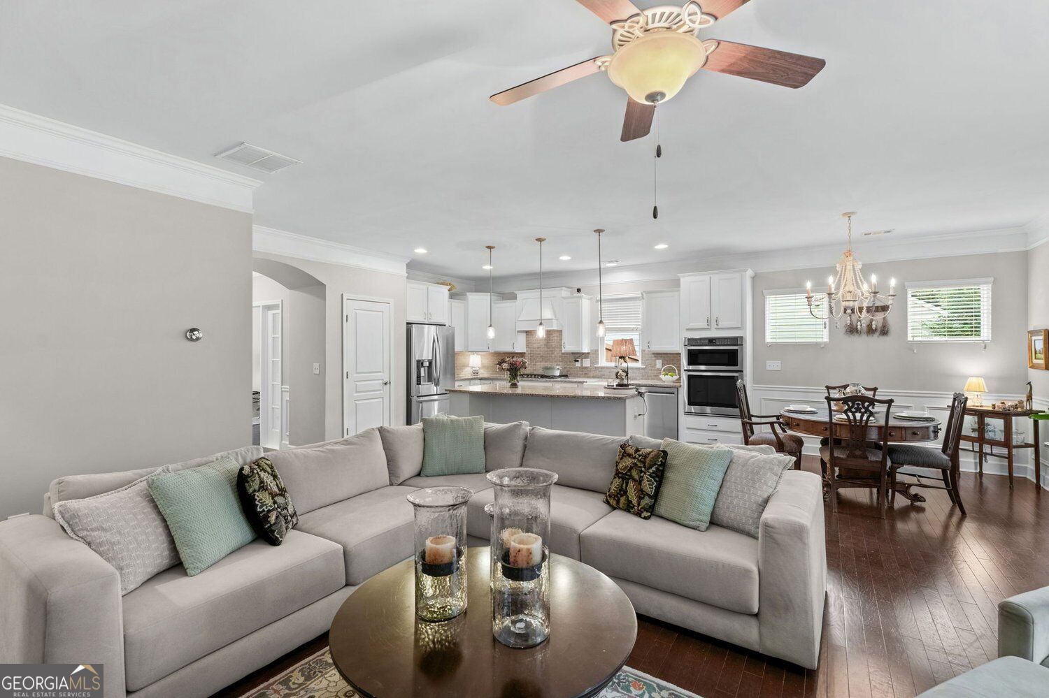 Open-plan living room with a large gray sectional, white kitchen, and dining area.
