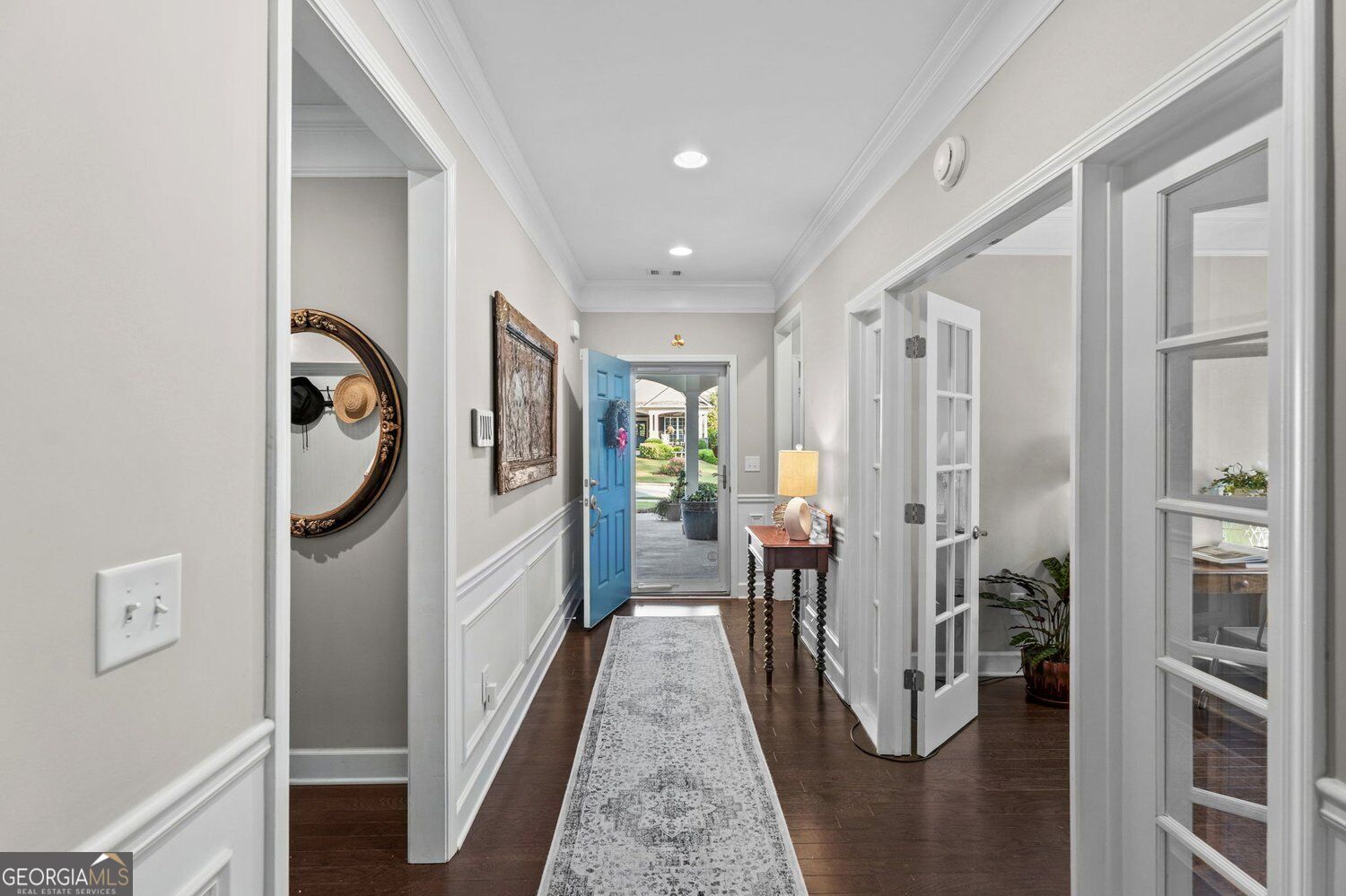 Entry hallway with dark hardwood floors, a patterned runner, and an open blue front door.