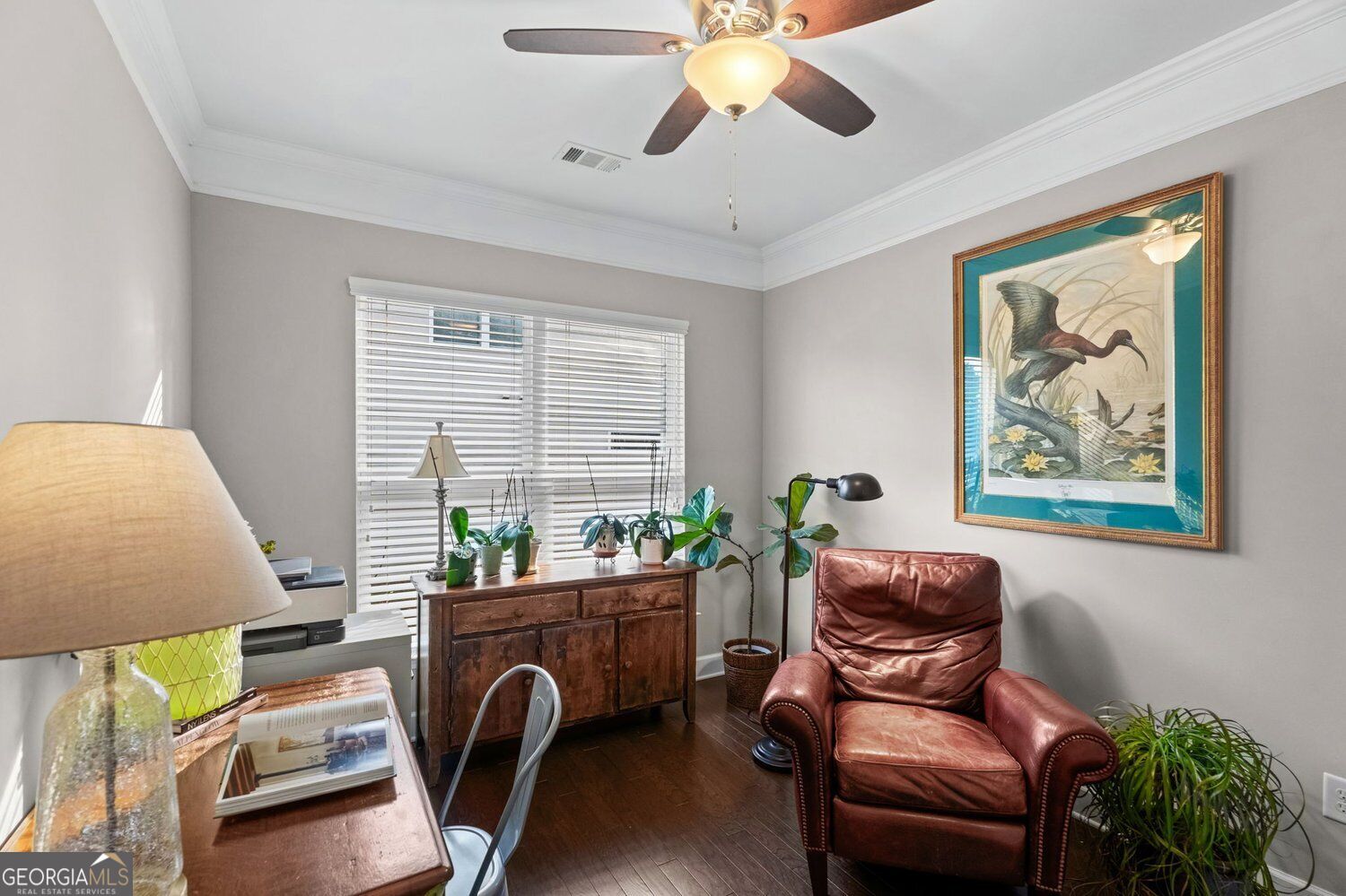 Furnished home office with a wooden desk, red leather armchair, and framed bird artwork.