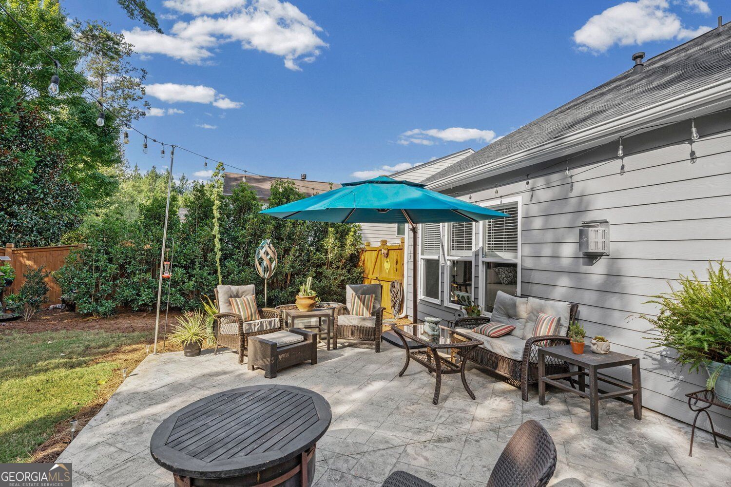 Backyard patio with wicker seating beneath a turquoise umbrella beside the gray-sided home.