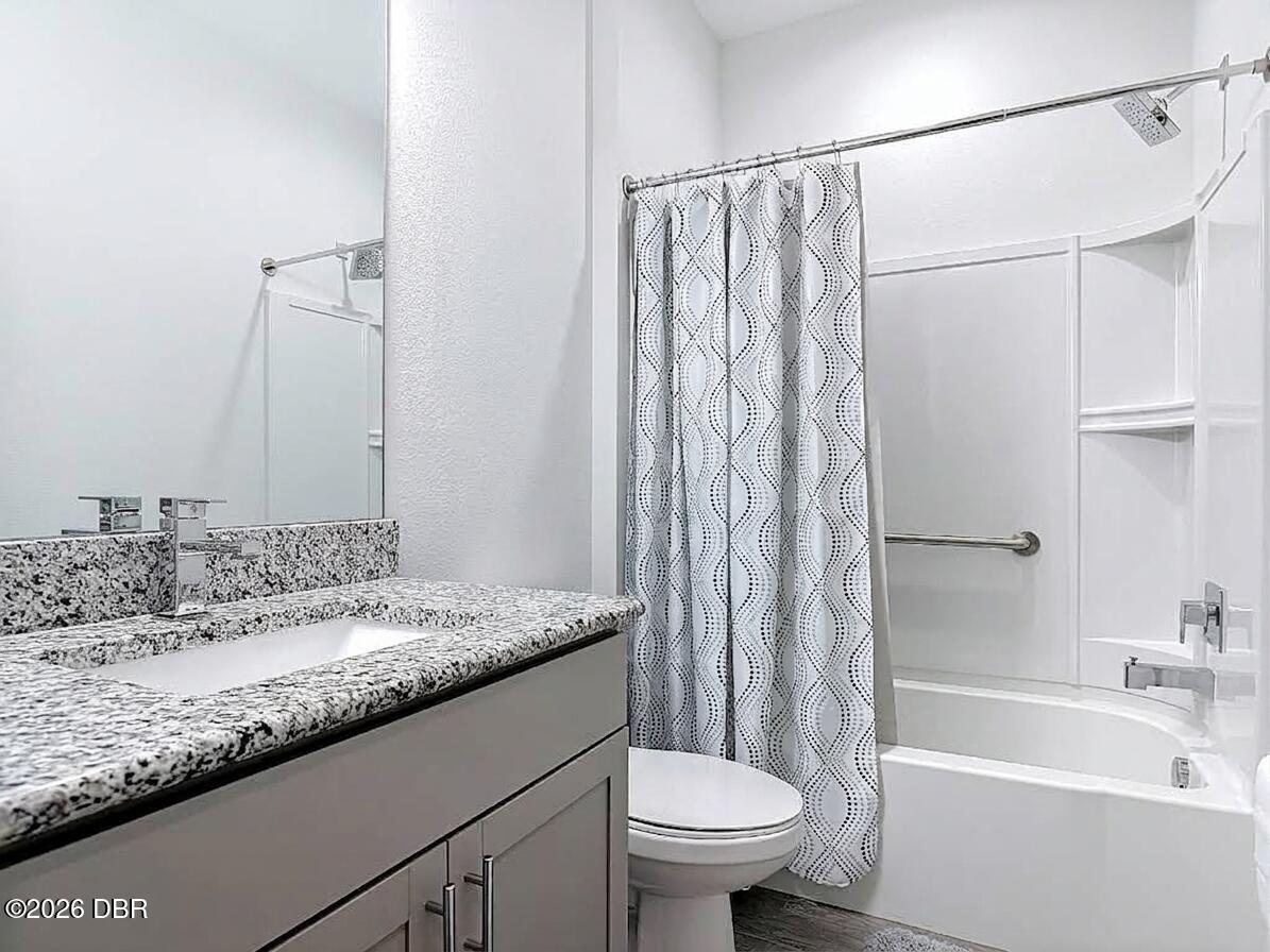Bathroom with a granite vanity, patterned shower curtain, bathtub, and built-in shelves.