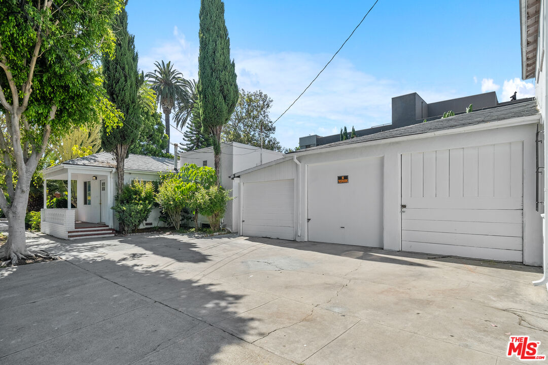 White garage buildings and a wide paved driveway framed by mature trees and palm trees.