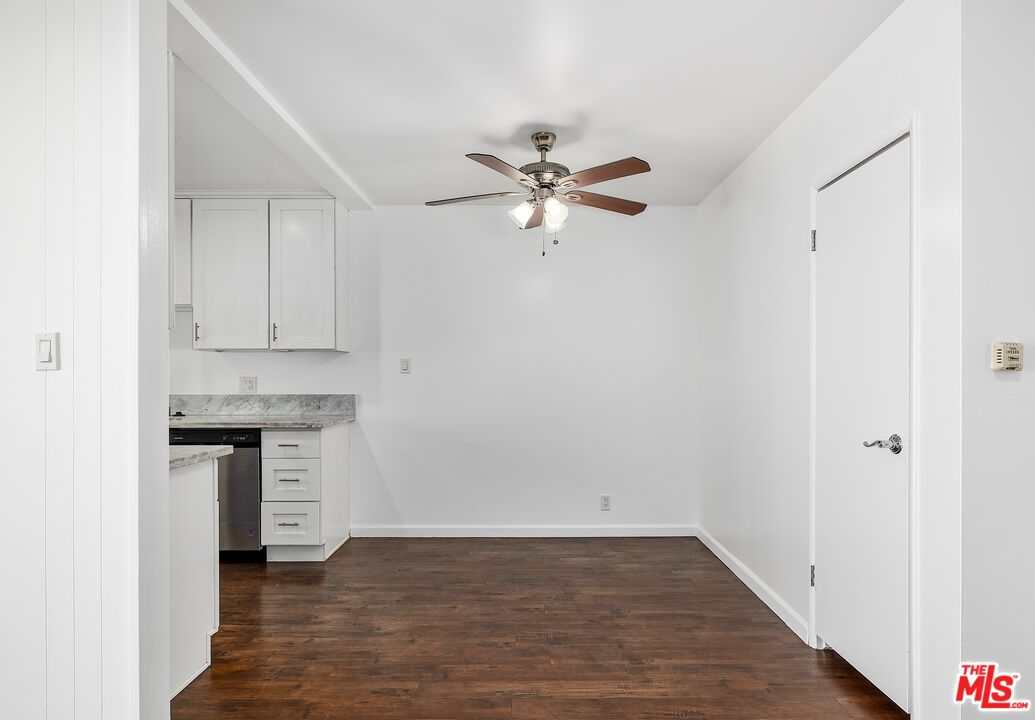 Unfurnished kitchen and dining area with white cabinets, stone counters, and dark wood flooring.