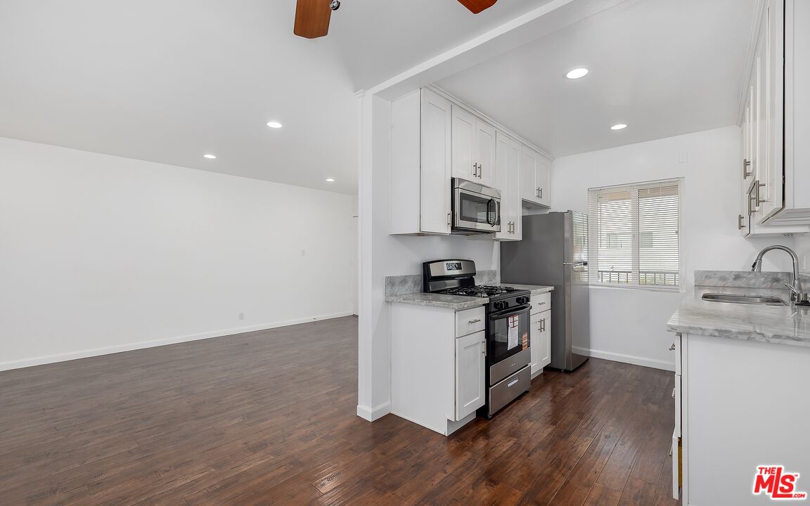 Open-plan apartment kitchen with white cabinetry, stainless steel appliances, and dark wood floors.