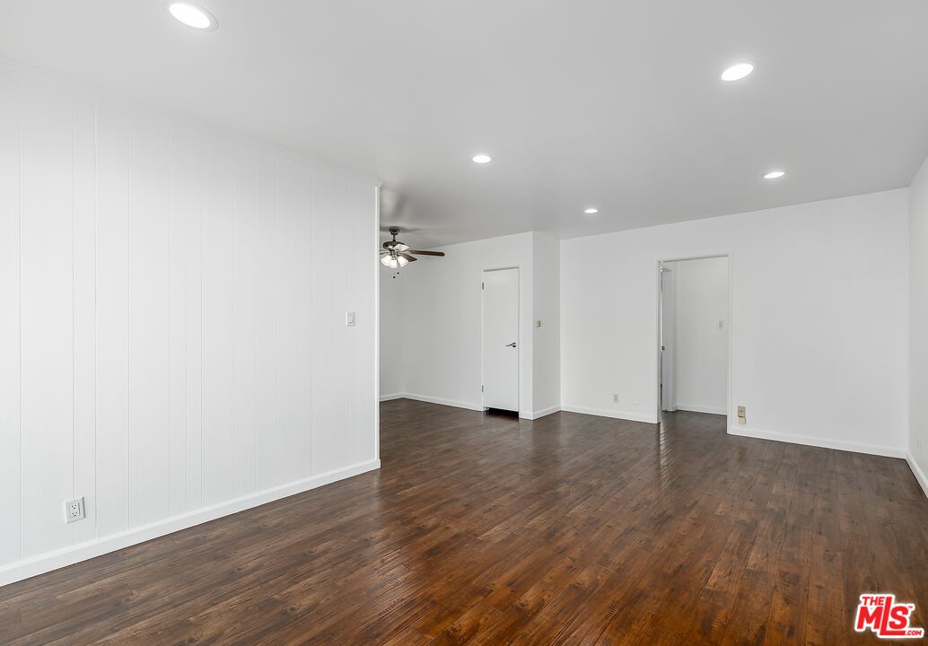 Empty room with dark wood flooring, white paneled walls, recessed lights, and a ceiling fan.