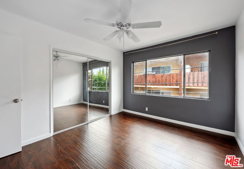 Empty bedroom with mirrored closet doors, dark wood flooring, and a charcoal accent wall.