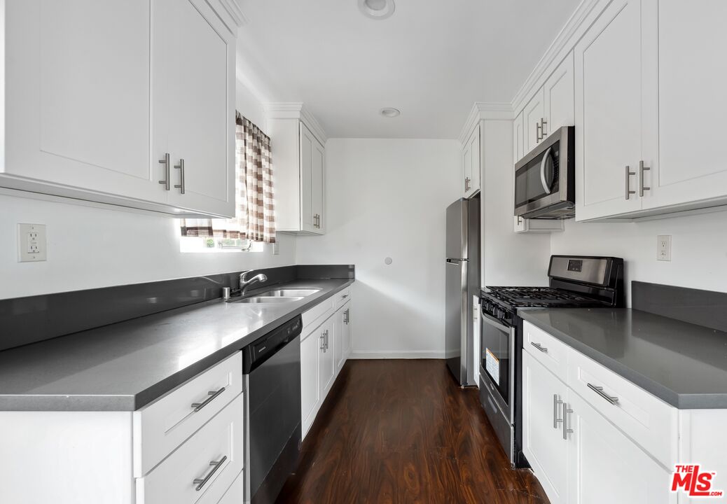 Galley kitchen with white cabinets, dark countertops, stainless steel appliances, and dark wood flooring.