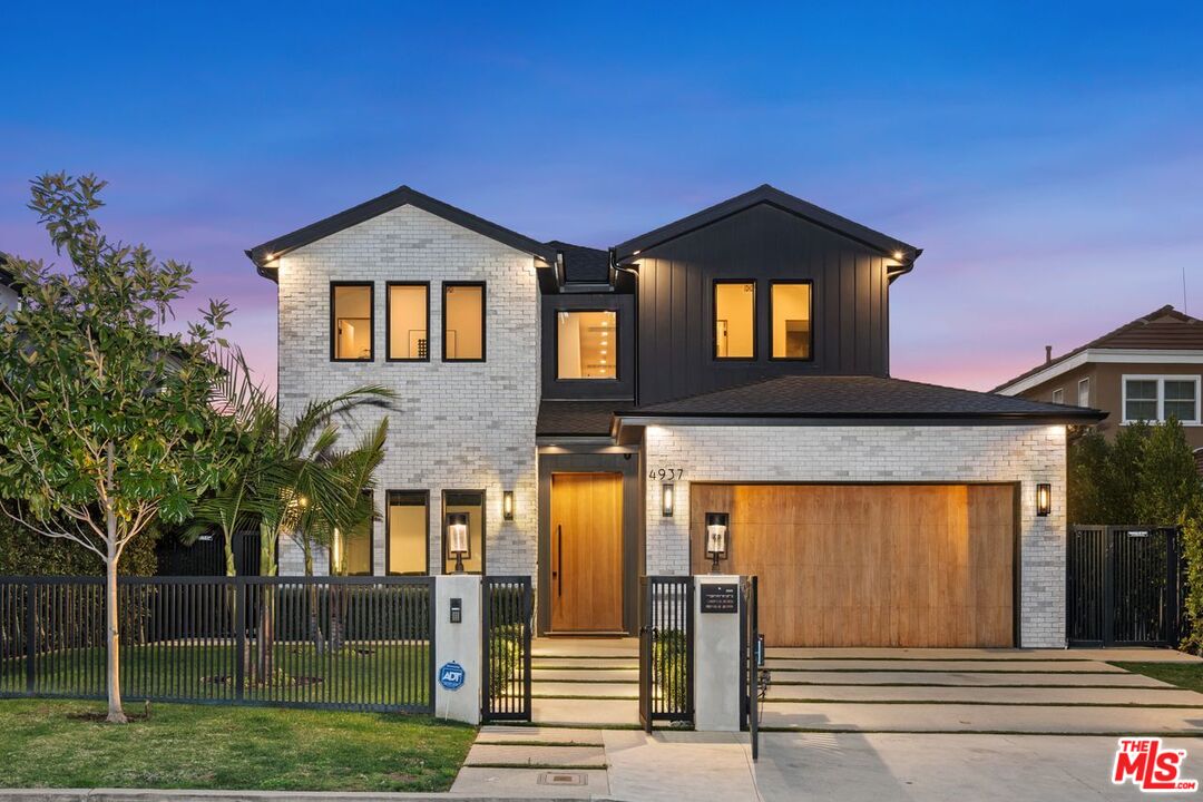 Modern two-story home with white brick, dark siding, and a wood garage door at dusk.