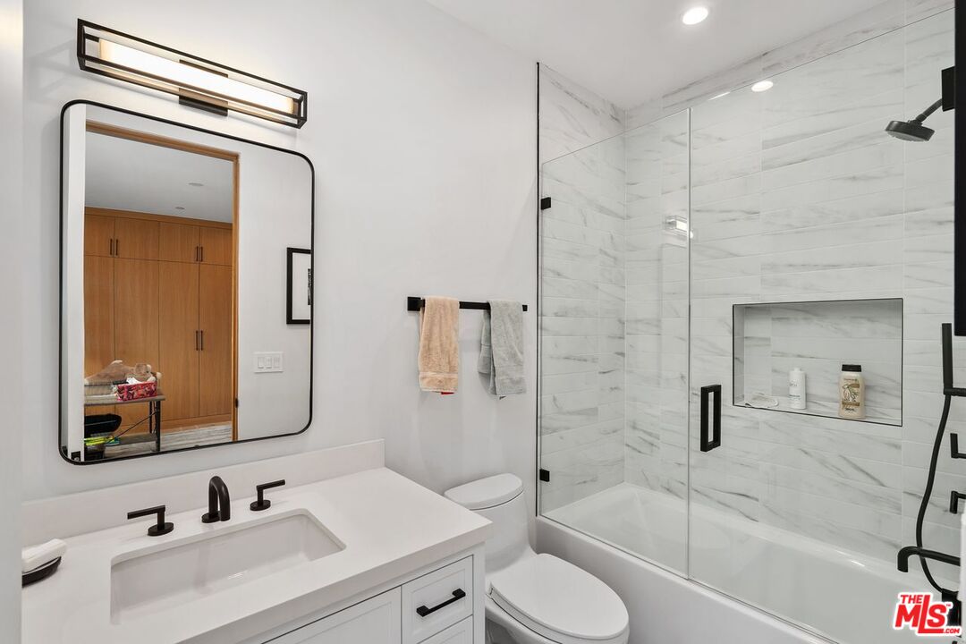 Renovated bathroom with a white vanity, black fixtures, and a glass-enclosed marble-look tub and shower.