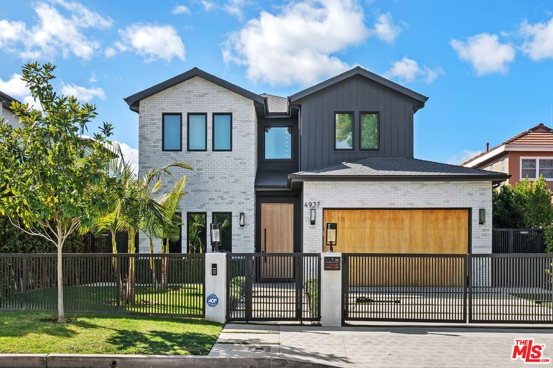 Modern two-story home with white brick, dark siding, a wood garage door, and a black metal front gate.