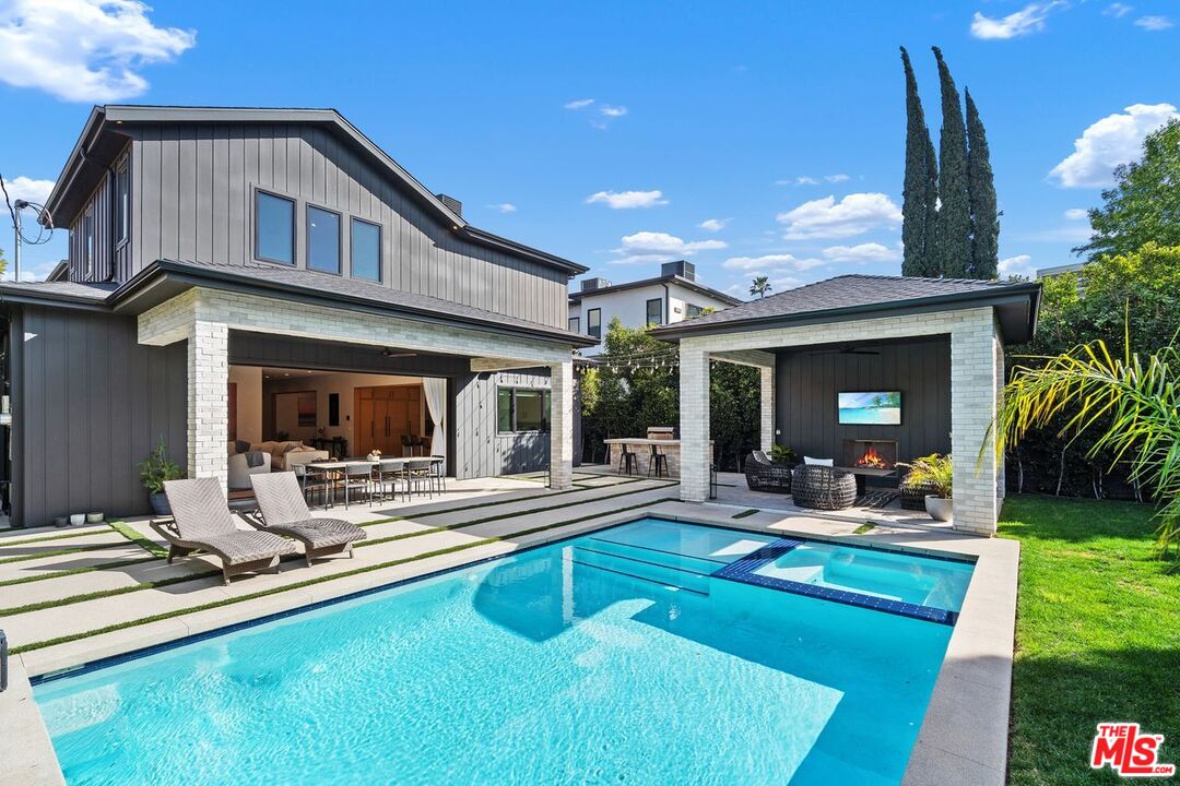 Modern home with a swimming pool, lounge chairs, and a covered patio with an outdoor fireplace.