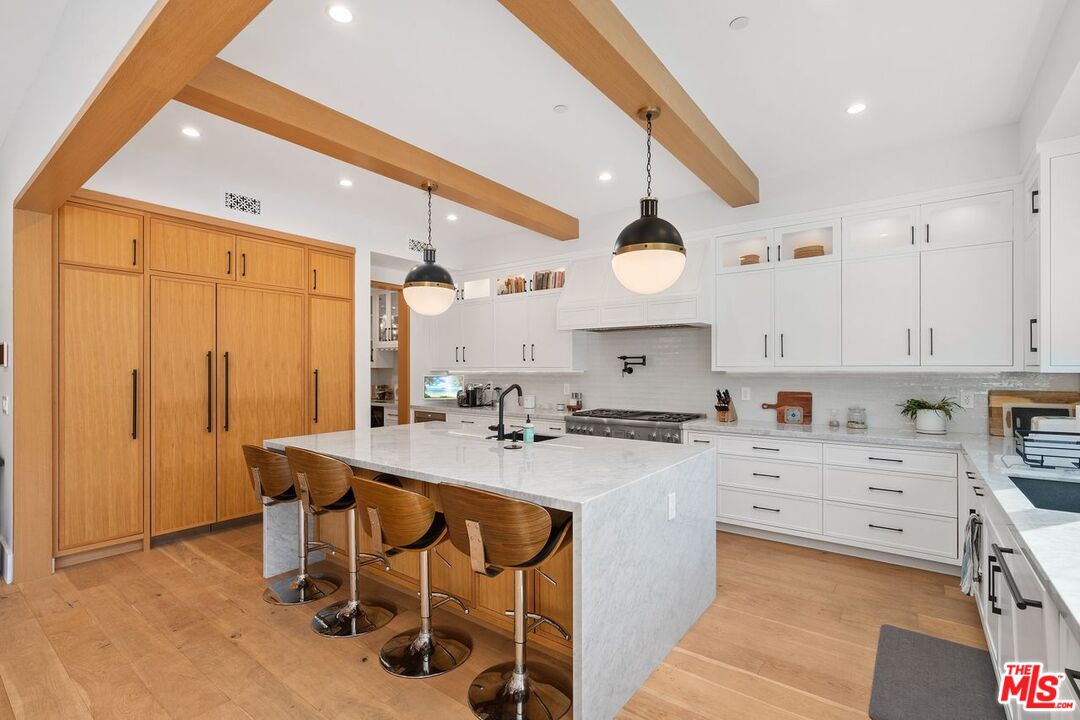 Modern kitchen with a large marble island, white cabinets, and exposed wood ceiling beams.