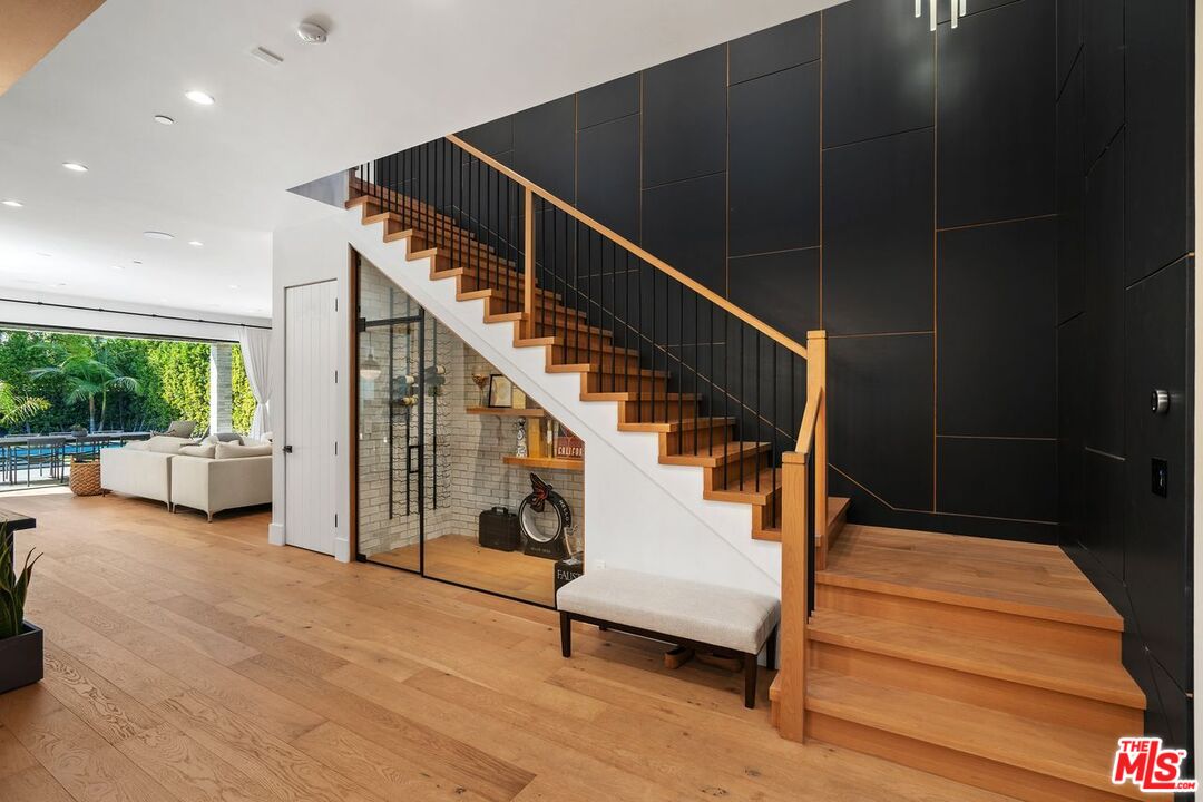 Modern foyer with a wood staircase, black paneled wall, and view into the living room.