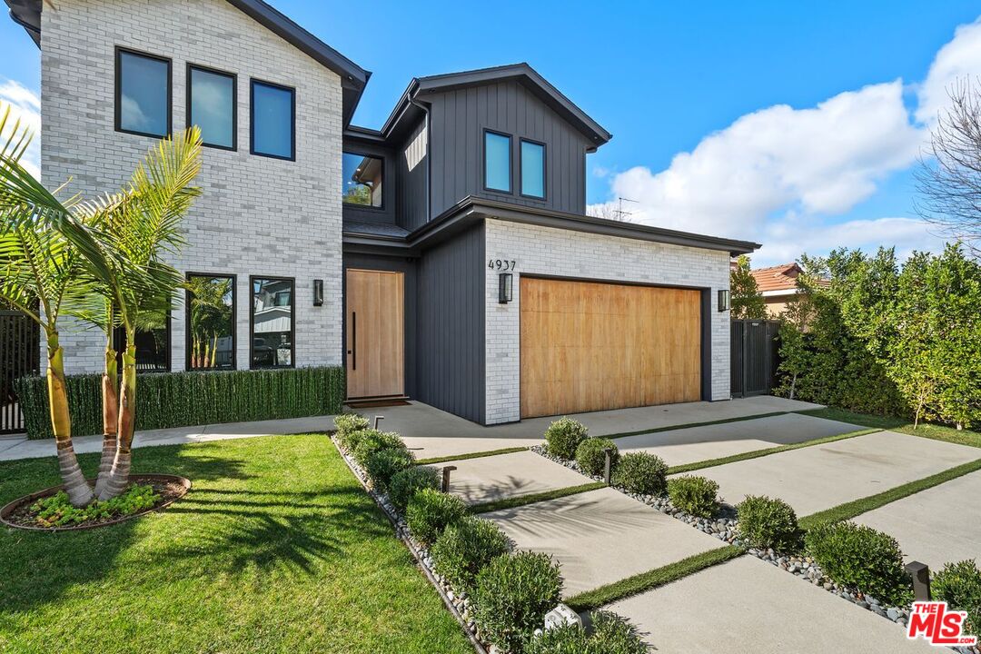 Modern two-story home with white brick, dark siding, and a wood garage door.