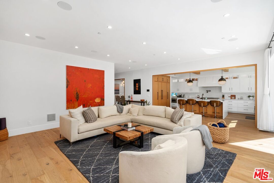 Open-plan living room with white seating, a red abstract painting, and an adjoining kitchen.