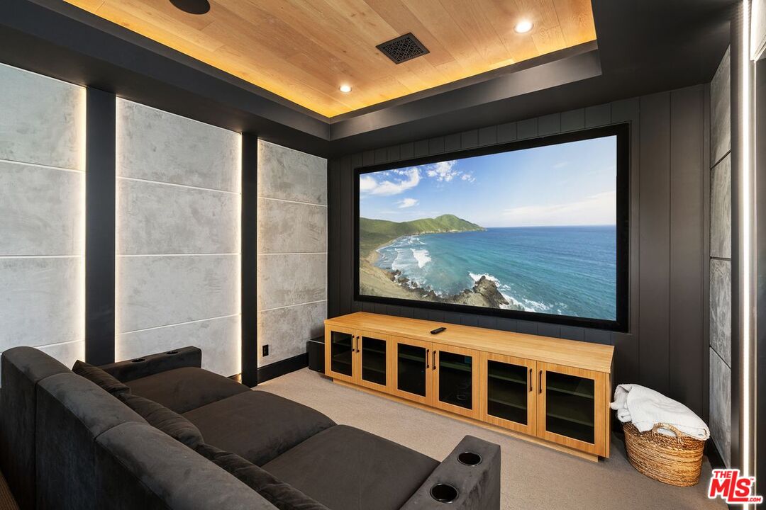 Home theater with a large coastal-scene screen, dark sectional, and warm wood ceiling.