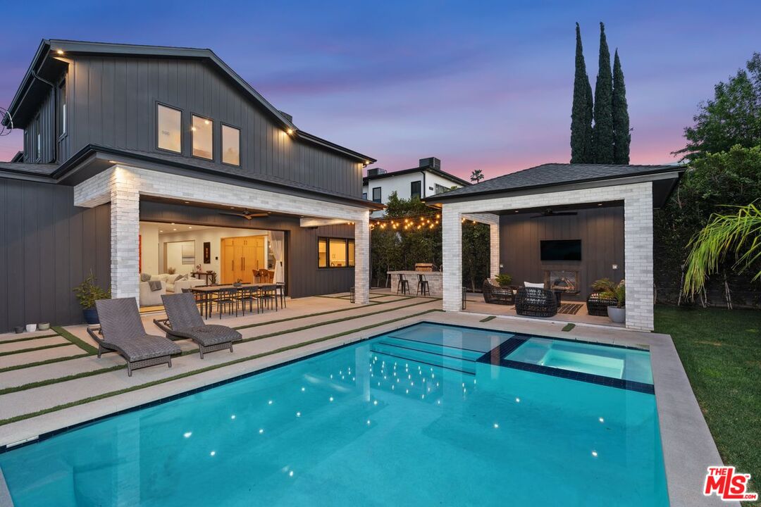Backyard pool beside a modern home, with a covered lounge pavilion and string lights at dusk.