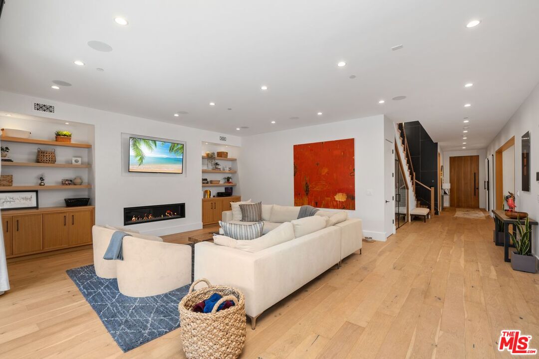 Living room with white sofas, a linear fireplace, built-in shelving, and light wood floors.