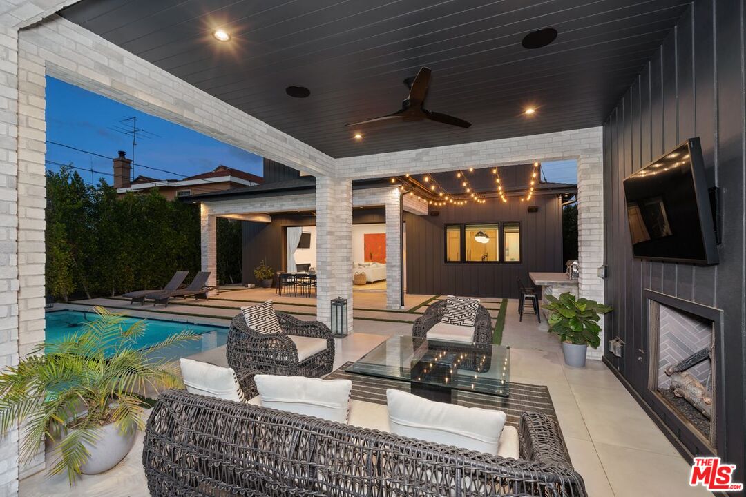 Covered patio with wicker seating beside a pool, lit by string lights at dusk.