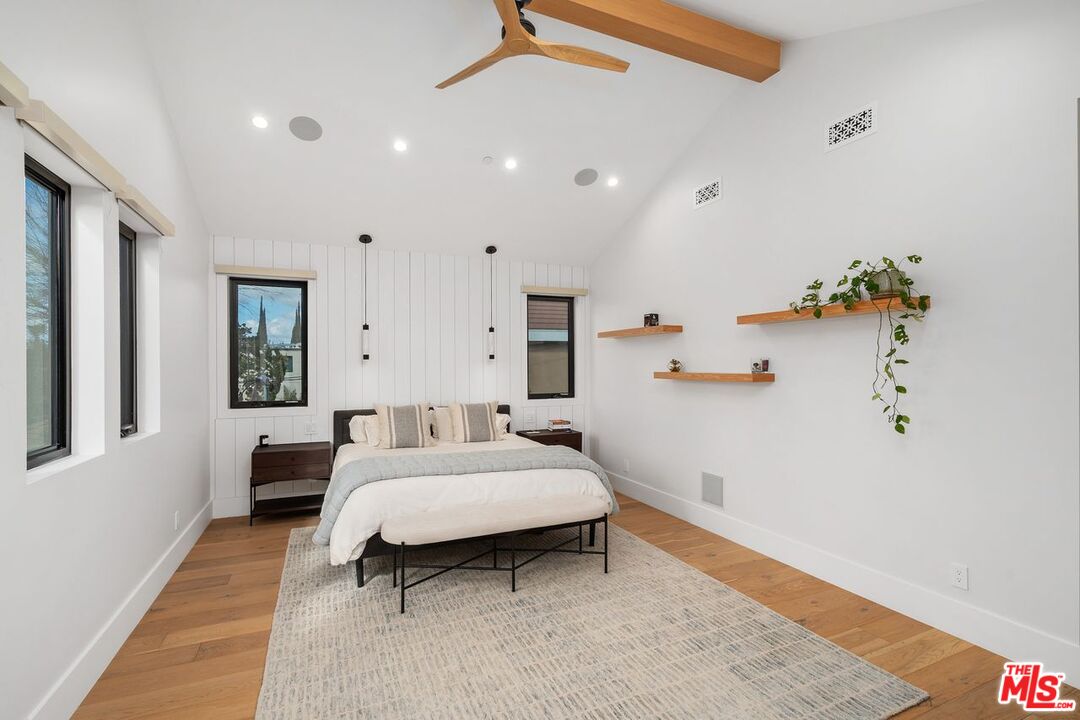 Bedroom with a low bed, white paneled walls, wide windows, and warm wood floors.