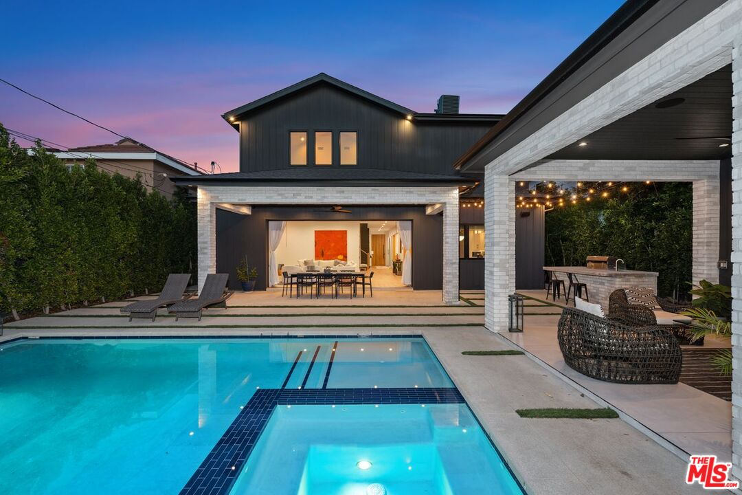 Modern home and covered patio behind a turquoise pool, with outdoor dining and string lights at dusk.