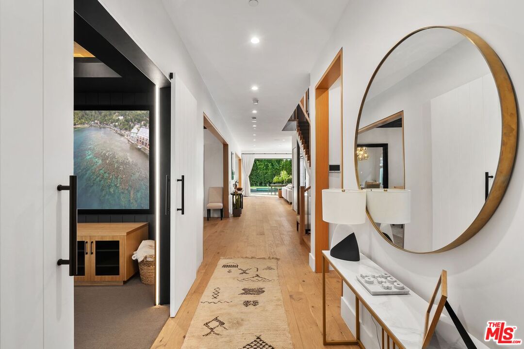 Contemporary entry hall with a round mirror, patterned runner, and backyard pool visible at the far end.