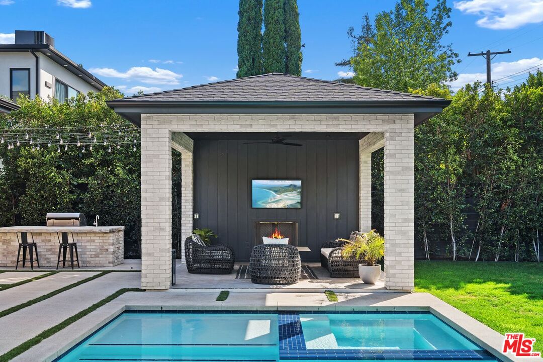 Backyard pool beside a brick cabana with a fireplace and furnished outdoor lounge.