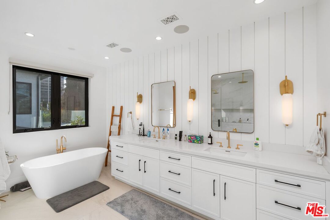 Modern bathroom with a freestanding tub and long double vanity with gold fixtures.