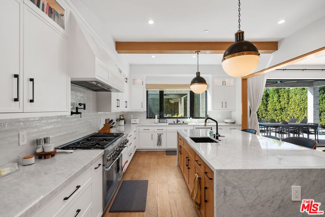 Modern kitchen with white cabinets, marble counters, and a large wood-paneled island opening to a patio.