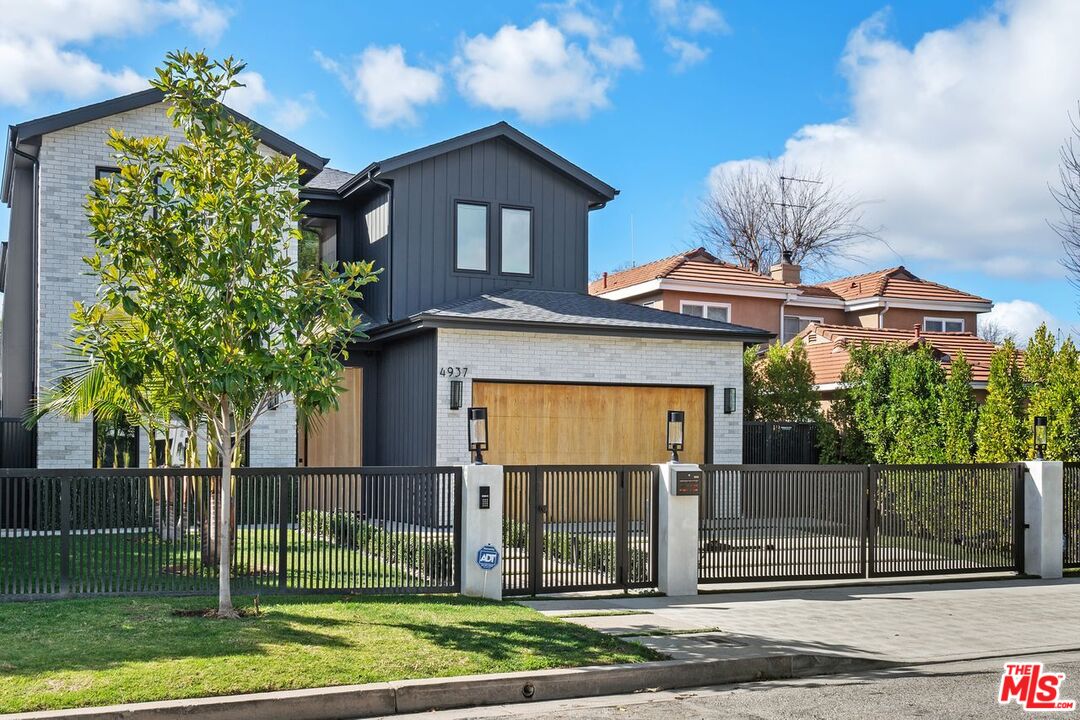 Modern two-story home with a wood garage door behind a black metal fence and gate.