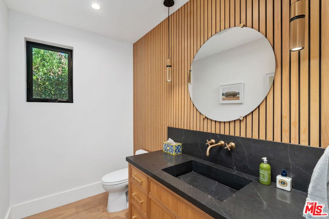 Bathroom with a black stone vanity, wood slat wall, round mirror, and brass fixtures.