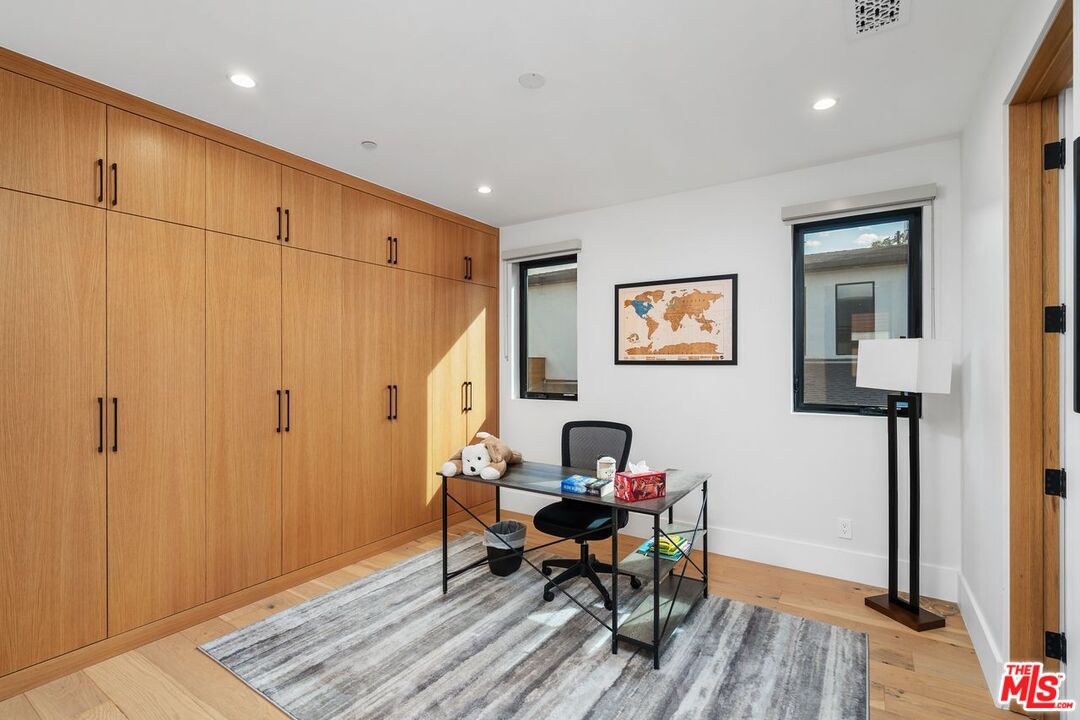Home office with extensive wood cabinetry, a desk, and a striped rug.