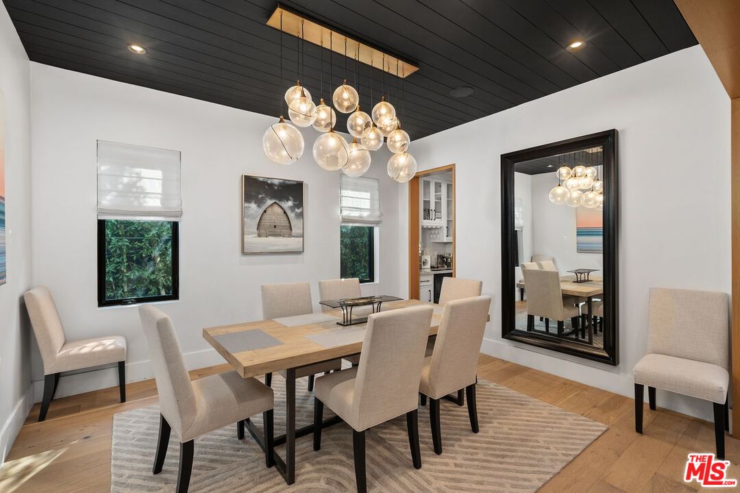Dining room with a light wood table, upholstered chairs, glass pendant lights, and a black paneled ceiling.