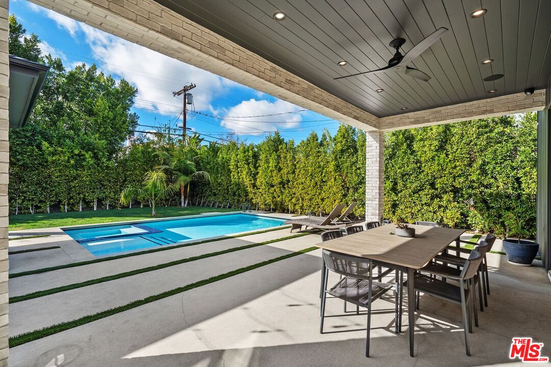 Backyard pool and spa beside a covered patio with outdoor dining furniture and tall hedges.