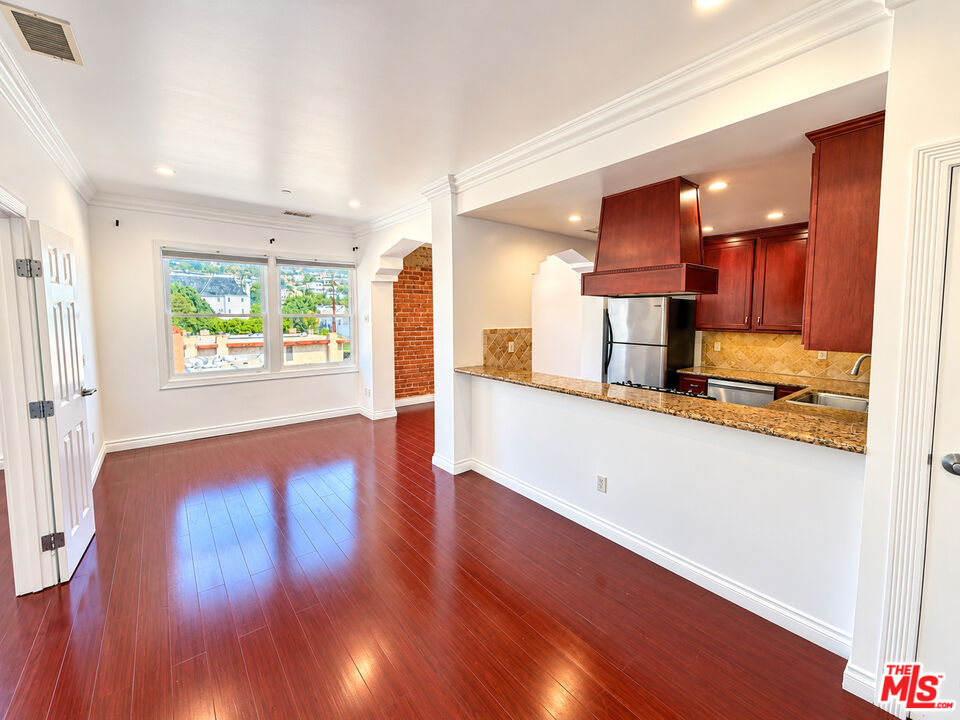Open kitchen and dining area with dark wood cabinets, a granite breakfast bar, and glossy red-toned floors.