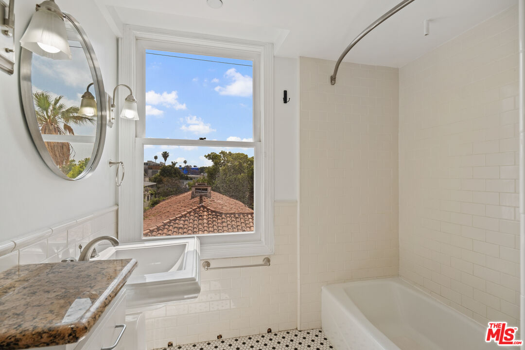 Bathroom with a white tub, mosaic tile floor, and a window overlooking trees and rooftops.