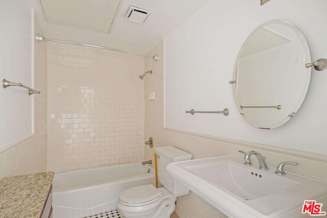 Bathroom with a white tub and tiled shower, toilet, and large sink beneath an oval mirror.