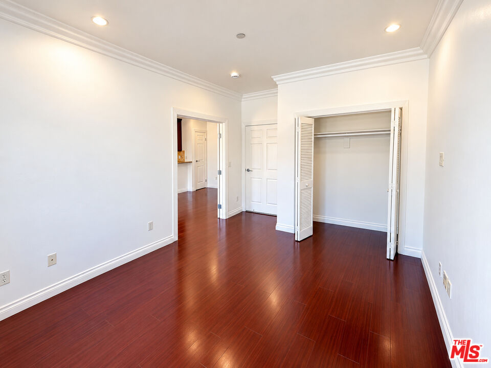 Empty room with reddish-brown wood flooring, crown molding, and an open closet with louvered doors.