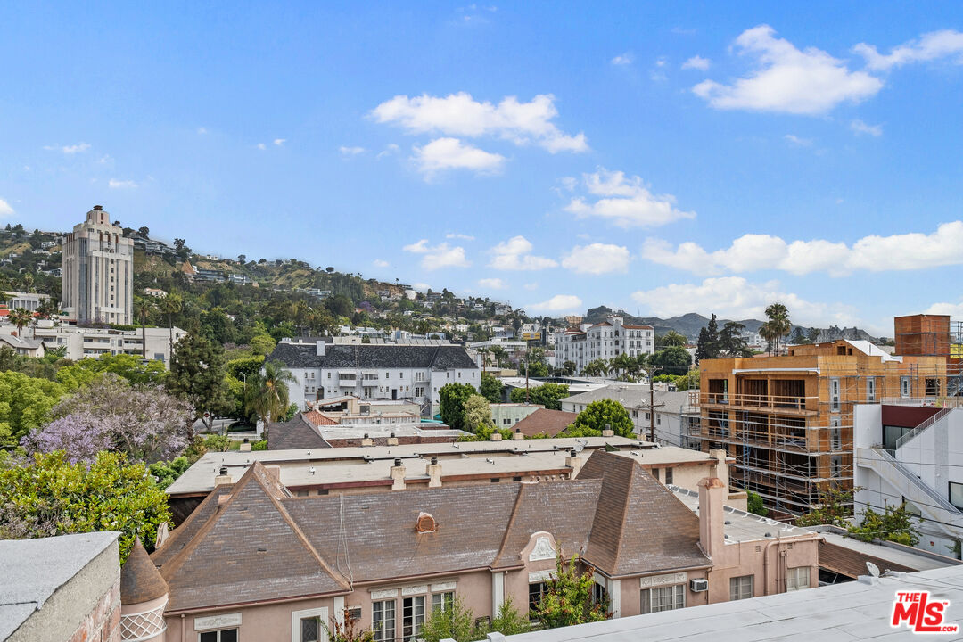 Panoramic view over West Hollywood rooftops, with hillside homes and a construction site.
