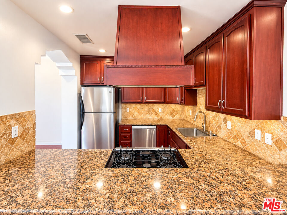 Kitchen with cherry-toned cabinets, granite counters, stainless steel appliances, and a gas cooktop in the island.