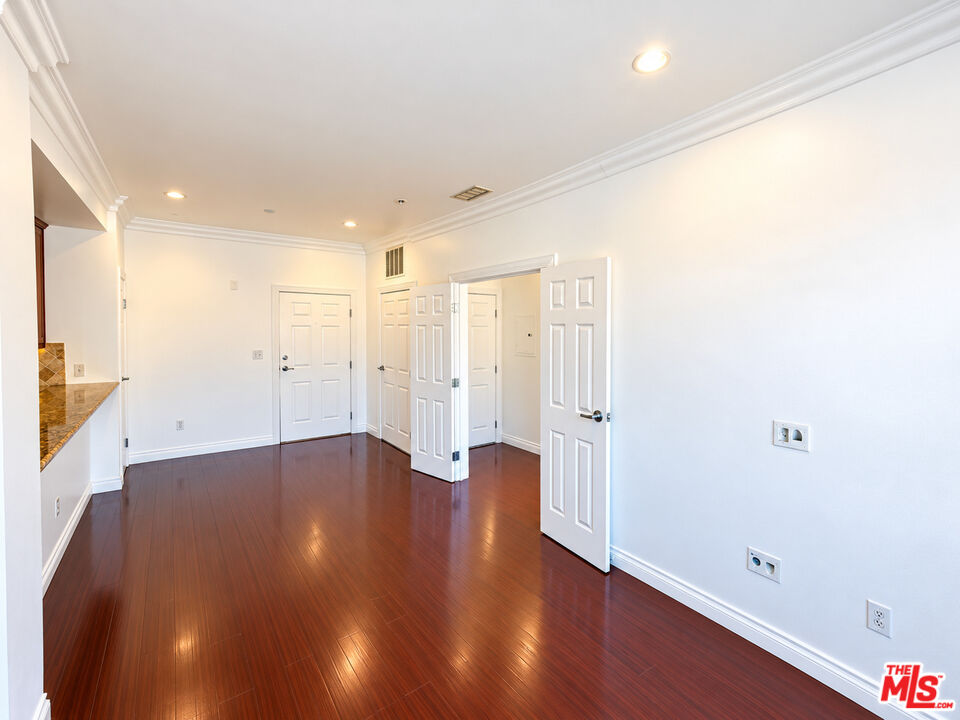 Unfurnished room with glossy hardwood floors, white walls, and several paneled doors.