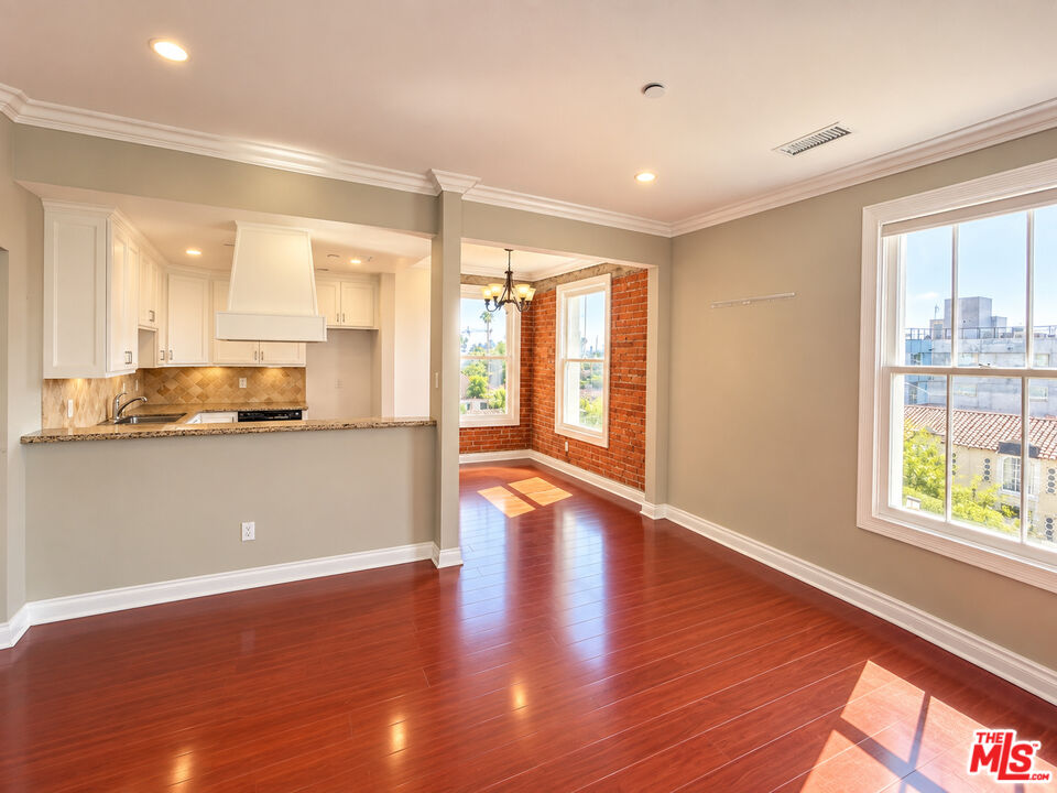 Open-plan kitchen and dining area with red hardwood floors, a brick accent wall, and large windows.