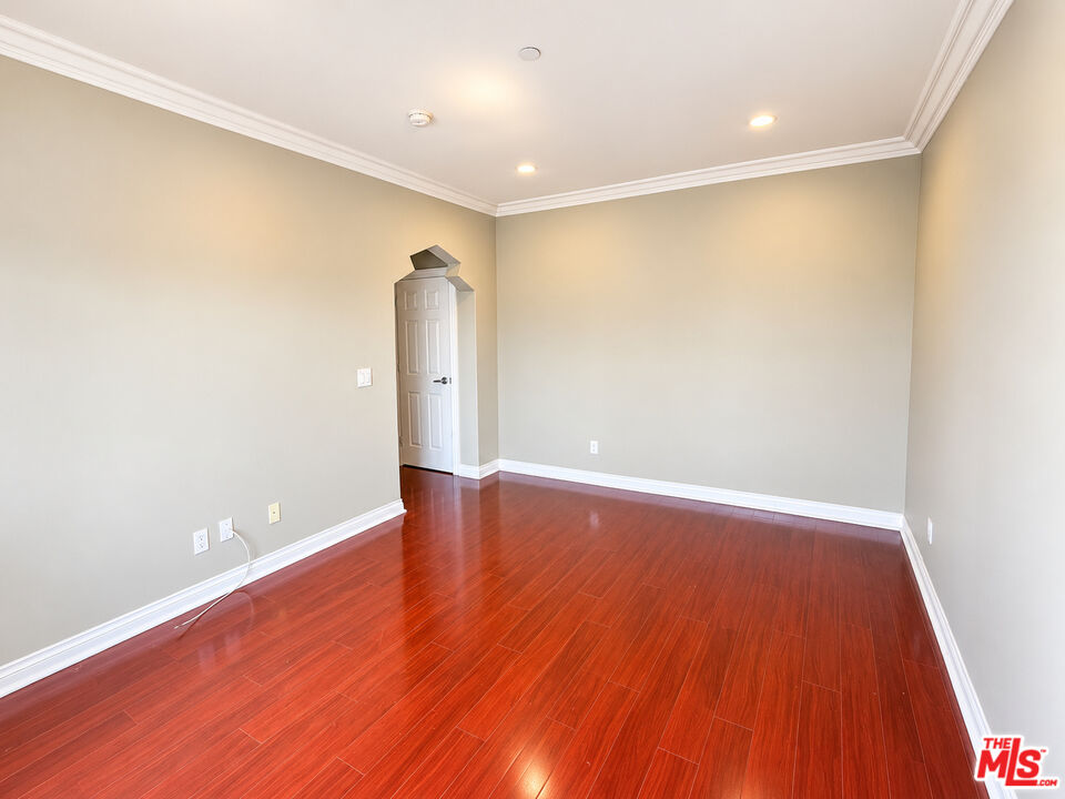 Empty room with glossy reddish-brown hardwood floors and white crown molding.