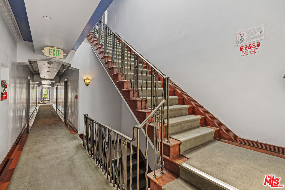 Building staircase beside a carpeted hallway, with dark wood trim and metal railings.
