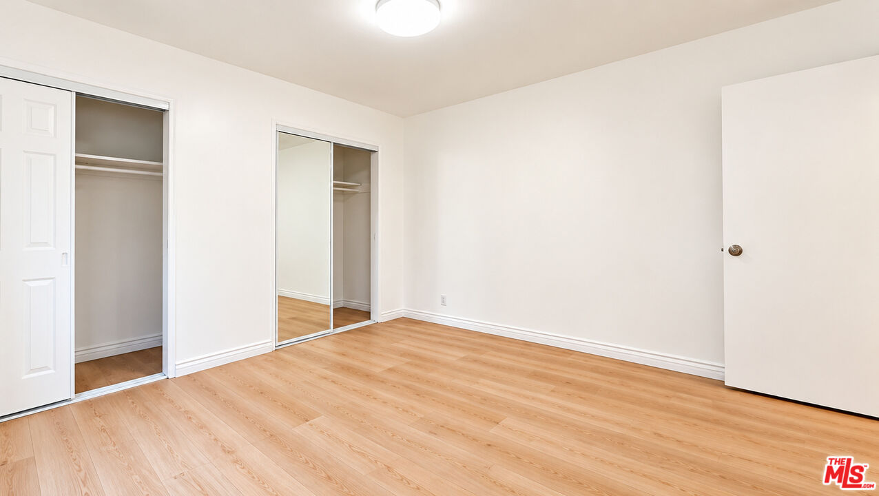 Empty bedroom with light wood floors and two closets, one with mirrored sliding doors.