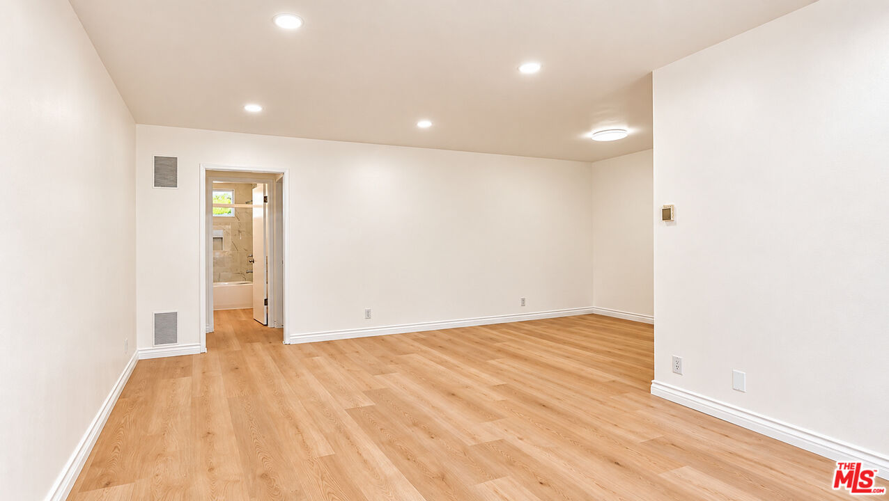Empty room with light wood floors and an open doorway to a bathroom.