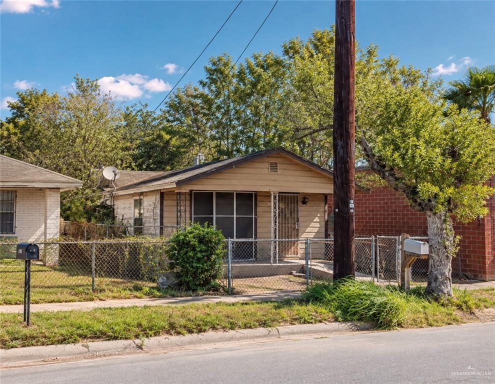 Single-story tan house with a covered porch behind a chain-link fence and utility pole.