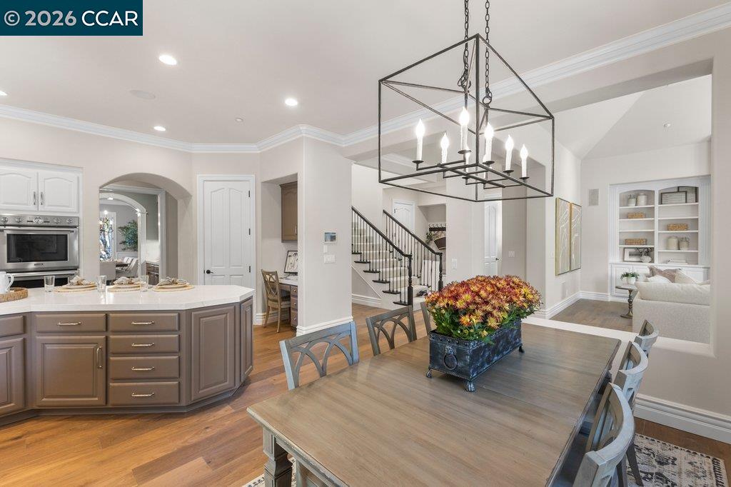 Open kitchen and dining area with a large island, chandelier, and staircase.