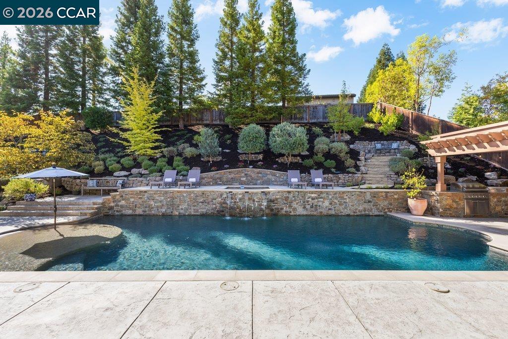 Backyard pool with stone retaining walls, landscaped hillside, and shaded seating areas.